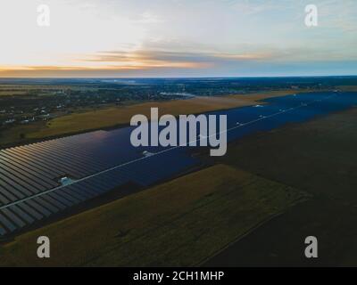 Luftdrohne Blick in große Sonnenkollektoren auf einer Solarfarm in großem Feld auf dem Land bei hellem Sonnenuntergang. Solarzellen Kraftwerke, bunte Foto Stockfoto