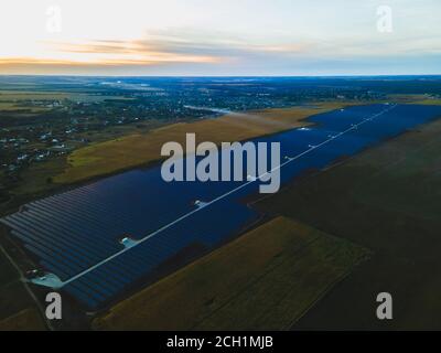 Luftdrohne Blick in große Sonnenkollektoren auf einer Solarfarm in großem Feld auf dem Land bei hellem Sonnenuntergang. Solarzellen Kraftwerke, bunte Foto Stockfoto