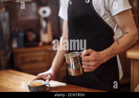 Nahaufnahme beschnittene Seitenansicht des Mannes, der Milch gießt Und bereiten Sie frischen Cappuccino zu Stockfoto