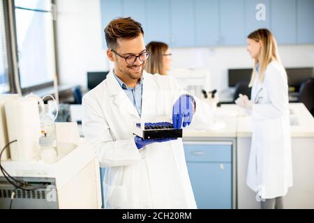 Handsome Forscher in schützende Arbeitskleidung stehen im Labor und Analyse von flüssigen Proben Stockfoto