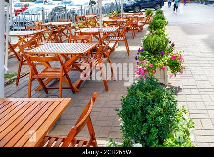 Die Holzmöbel des Straßencafés sind vor dem Hintergrund des Bürgersteiges der Stadt und eines Teils der Straße mit vorbeifahrenden Autos verlassen. Stockfoto