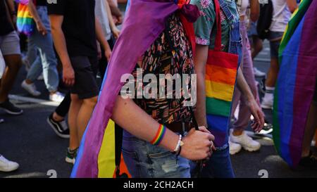 gleichstellungsmarsch der LGBT. Zwei Schwule halten die Hände und gehen stolz Parade. Junge Menschen in Regenbogenkleidung und Symbolen kämpfen für LGBTQ+-Rechte. Stockfoto