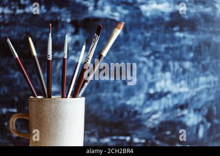 Malpinsel in einem Keramikbecher vor einem blauen abstrakten Hintergrund. Stockfoto