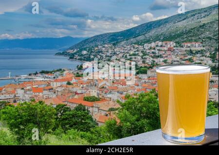 Ein Glas helles Bier gegen den Blick von oben auf Senj Stadt, Kroatien. Blick von der Festung Nehaj, Festung auf dem Hügel, Velebit, Kroatien. Stockfoto