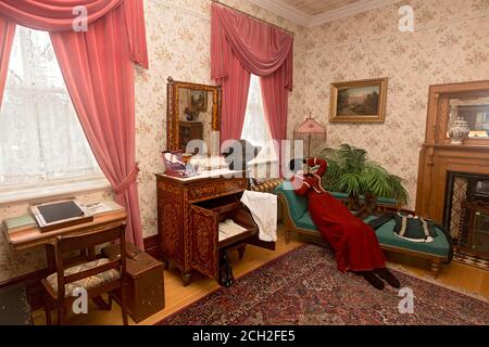 Das erste Gästeschlafzimmer im Regierungsgebäude in Regina, Saskatchewan, Kanada, war für die wichtigsten Gäste reserviert.das Haus diente bis 1945 als offizieller Wohnsitz der Vizegouverneure der NW-Territorien und später der Provinz Saskatchewan. Die Einrichtung und Kleidung werden ausgewählt, um die Zeit des Vizegouverneurs Amedee Forget (1898-1910) zu repräsentieren. Die "Ohnmachtsliege" wurde von Frauen benutzt, da sie nach ihrem 13. Lebensjahr so enge Korsetts (auf dem Fußhocker zu sehen) trugen, dass es oft schwer war, den Atem zu fangen. Eigentumsfreigabe nicht erforderlich, da dieses Museum im Besitz des C ist Stockfoto