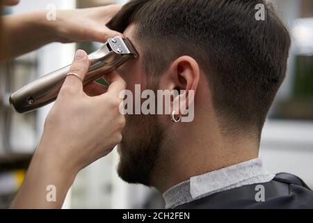 Schöne kaukasische Frau Friseursalon Frisur für Kunden. Nahaufnahme Portrait weiblicher barber mit Frisierwerkzeugen Trimmer bei der Arbeit. Haarschnitt Stockfoto