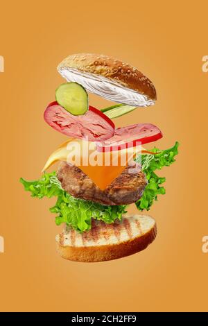 Burger mit fliegenden Zutaten isoliert auf orangefarbenem Hintergrund Stockfoto