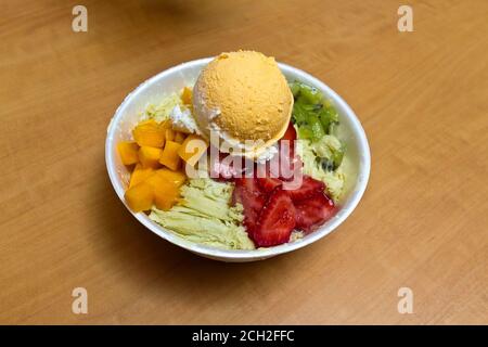 Frappe, ein sehr beliebtes asiatisches Sommergericht mit aromatisiertem rasierten Eis mit Früchten und oft einer Kugel Eis. Dies ist Grüntee-Eis mit Mango und Erdbeeren zusammen mit Mango-Eis. Stockfoto