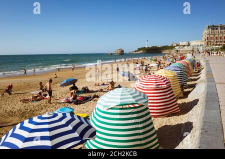 Biarritz, Französisch Baskenland, Frankreich - 19. Juli 2019 : Strandgänger unter bunten Sonnenschirmen am La Grande Plage, dem größten Strand der Stadt. Hôtel d Stockfoto