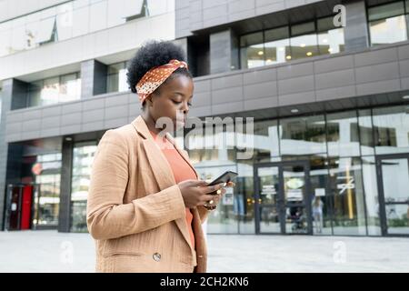 Junge seriöse Geschäftsfrau der afrikanischen Ethnizität Scrollen im Smartphone Stockfoto