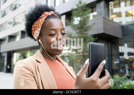 Glückliche junge afrikanische Geschäftsfrau mit Kopfhörern, die durch Video-Chat sprechen Stockfoto