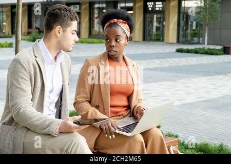 Junger seriöser Geschäftsmann mit Tablet, der seiner afrikanischen Frau zuhört Kollege Stockfoto