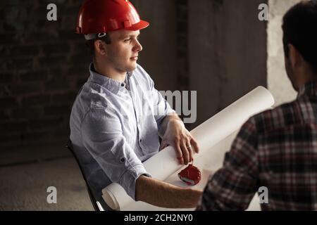 Nachdenklicher Ingenieur in rotem Hut zählt die Fliegen. Nahaufnahme Seitenansicht Foto. Denkprozess Stockfoto