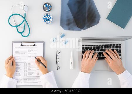 Flatlay der Hände von zwei Klinikern, die medizinische Notizen und Tippen mit dem Laptop Stockfoto