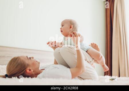 Junge Mutter spielt mit ihrem neugeborenen Sohn zu Hause. Familie hat Spaß auf dem Bett im Schlafzimmer liegen Stockfoto