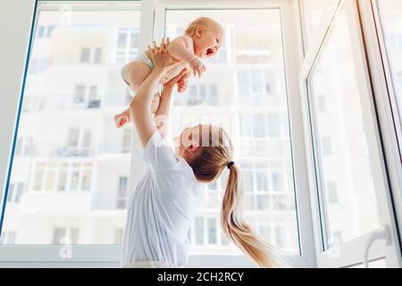 Mutter spielt mit neugeborenem Sohn zu Hause. Frau wirft das Kind auf den Balkon. Glückliches Kleinkind trägt Windel Stockfoto