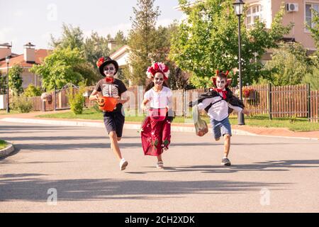 Drei fröhliche Kinder in halloween-Kostümen halten Behälter mit süßen Leckerbissen Stockfoto