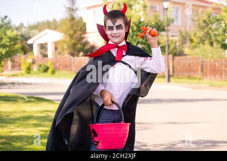 Lächelnder Junge im halloween Kostüm des Teufels mit Hörnern an Sein Kopf hält Leckereien Stockfoto