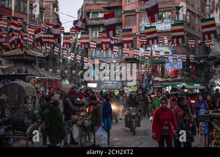 Kathmandu, Nepal - Dezember 22 2019:Unidentifizierte Menschen laufen und fahren durch verschiedene Geschäfte und Straßenhändler auf der Straße mit bunten Fahnen oben Stockfoto