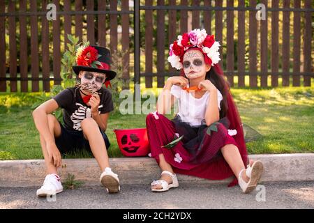 Freundliche Mädchen und Jungen in halloween-Kostüme sitzen auf der Straße Vor der Kamera Stockfoto