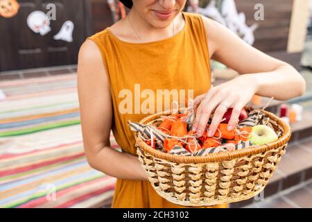 Junge elegante Frau in gelbem Kleid hält Korb mit halloween Leckerbissen Stockfoto