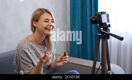 Ein Beauty-Blogger oder Video-Blogger erzählt und zeigt Abonnenten, wie man Make-up macht. Junge Frau malt Lippen und lacht über einen Witz Stockfoto