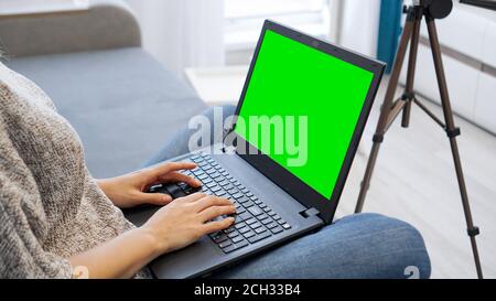 Bloggerin, die am Laptop arbeitet. Ansicht der Kamera auf Stativ und Laptop mit grünem Bildschirm Chromakey - Nahaufnahme Stockfoto