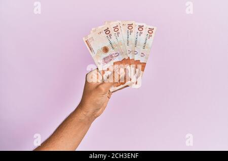 Hispanische Hand mit 10 kolumbianischen Pesos-Banknoten auf isoliertem rosa Hintergrund. Stockfoto