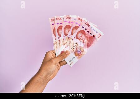 Hispanische Hand mit 100 chinesischen Yuan-Banknoten auf isoliertem rosa Hintergrund. Stockfoto