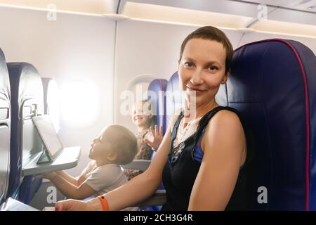 Junge Erwachsene schöne attraktive kaukasische Mutter Reisen mit niedlichen kleinen liebenswert Geschwister Junge und Mädchen im Flugzeug. Mutter Tochter und Sohn sitzen drinnen Stockfoto