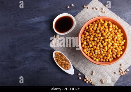 Gebratene Kichererbsen mit Gewürzen in einem Tonteller auf schwarzem Holzhintergrund, Draufsicht, Kopierraum. Stockfoto