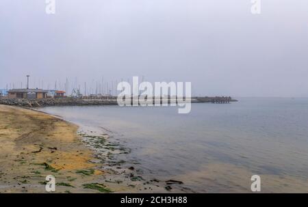 Blick auf einen Sandstrand am Pazifik und einen Angelpier in Pillar Point Half Moon Bay in der Nähe von San Francisco an einem nebligen Tag, mit Booten im Hintergrund Stockfoto