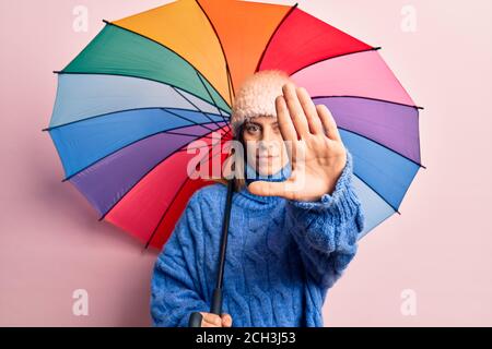 Junge schöne Frau hält bunten Regenschirm mit offener Hand tun Stop-Zeichen mit ernsten und selbstbewussten Ausdruck, Verteidigung Geste Stockfoto