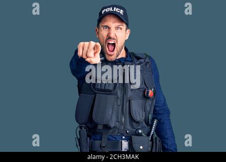 Junger gutaussehender Mann in Polizeiuniform zeigt unzufrieden und frustriert auf die Kamera, wütend und wütend auf Sie Stockfoto