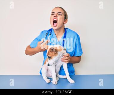 Junge schöne blonde Tierärztin Putting Impfstoff Welpen Hund wütend und verrückt schreien frustriert und wütend, schreien mit Wut. Wut und ein Stockfoto