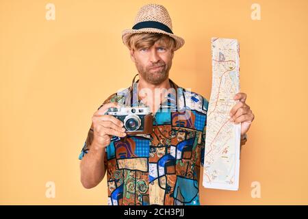 Junge blonde Mann hält vintage Kamera und Stadtplan deprimiert und sorgen für Not, Weinen wütend und Angst. Trauriger Ausdruck. Stockfoto