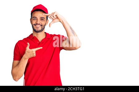 Junge gut aussehende hispanischen Mann trägt Lieferung Kurier uniform lächelnd machen Rahmen mit Händen und Fingern mit glücklichem Gesicht. Kreativität und Fotografie c Stockfoto