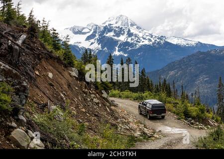 Modernes Fahrzeug, das auf kurviger Forststraße in der Nähe von rauer Hanglage während der Fahrt durch verschneite Berge in British Columbia, Kanada, fährt Stockfoto