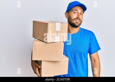 Schöner Mann mit Bart tragen Kurier Uniform halten Lieferpakete suchen schläfrig und müde, erschöpft für Müdigkeit und Kater, faule Augen in t Stockfoto