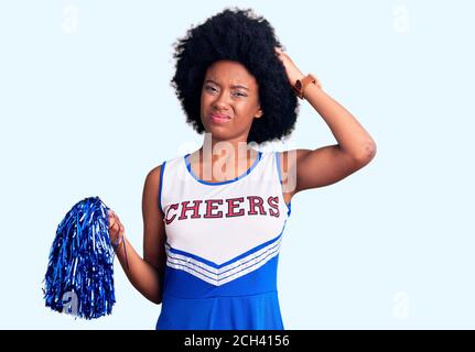 Junge afroamerikanische Frau trägt Cheerleader Uniform hält Pompon verwirren und fragen sich über Frage. Unsicher mit Zweifel, Denken mit der Hand Stockfoto