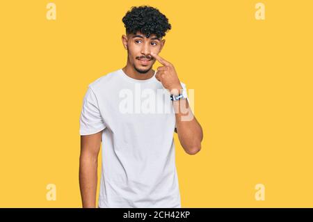 Junger arabischer Mann trägt lässige weiße T-Shirt zeigt mit der Hand Finger auf Gesicht und Nase, lächelnd fröhlich. Beauty-Konzept Stockfoto