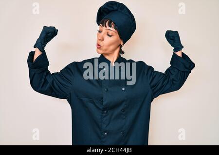 Schöne brunettte Frau trägt professionelle Koch Uniform zeigt Arme Muskeln lächelnd stolz. Fitness-Konzept. Stockfoto