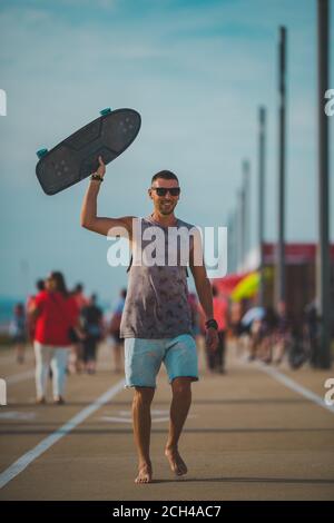 Glücklich sorglos sportlich Mann genießen das Leben und Walking mit Longboard in der Hand auf Sonnenuntergang. Sommeraktivitäten Konzept Stockfoto