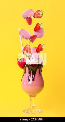 Glas leckeren Erdbeermilchshake und herabfallende Zutaten auf Farbe Hintergrund Stockfoto