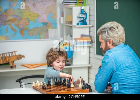 Vatertag. Glückliches kleines Kind, das Schach mit einem älteren Mann zu Hause spielt. Kinder Spielen Schach. Vater und Sohn spielen Schach. Hauslehrer hilft Jungen mit Stockfoto