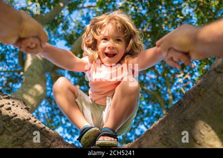 Vater hilft Sohn klettern einen Baum. Glücklicher Junge, der im Sommer einen Baum klettert. Vaterhand. Kinderschutz. Stockfoto