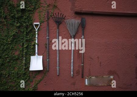 Die Gartengeräte hängen an der roten Zementwand. Stockfoto