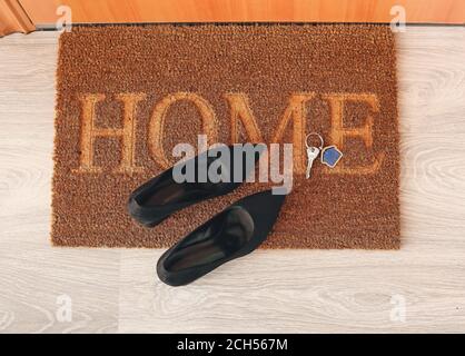 Türmatte mit Schlüssel aus dem Haus und Schuhe auf dem Boden Stockfoto