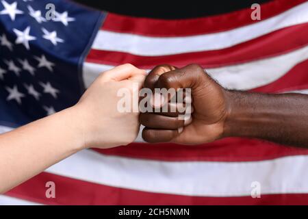 Kaukasische Frau und afroamerikanischer Mann, der die Fäuste in der Nähe der Nationalflagge der USA anstößt. Rassismus-Konzept Stockfoto