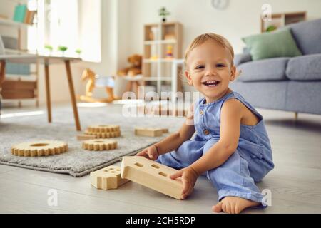 Niedliches kleines Kind, das beim Spielen lächelnd auf die Kamera schaut Im gemütlichen Kinderzimmer Stockfoto